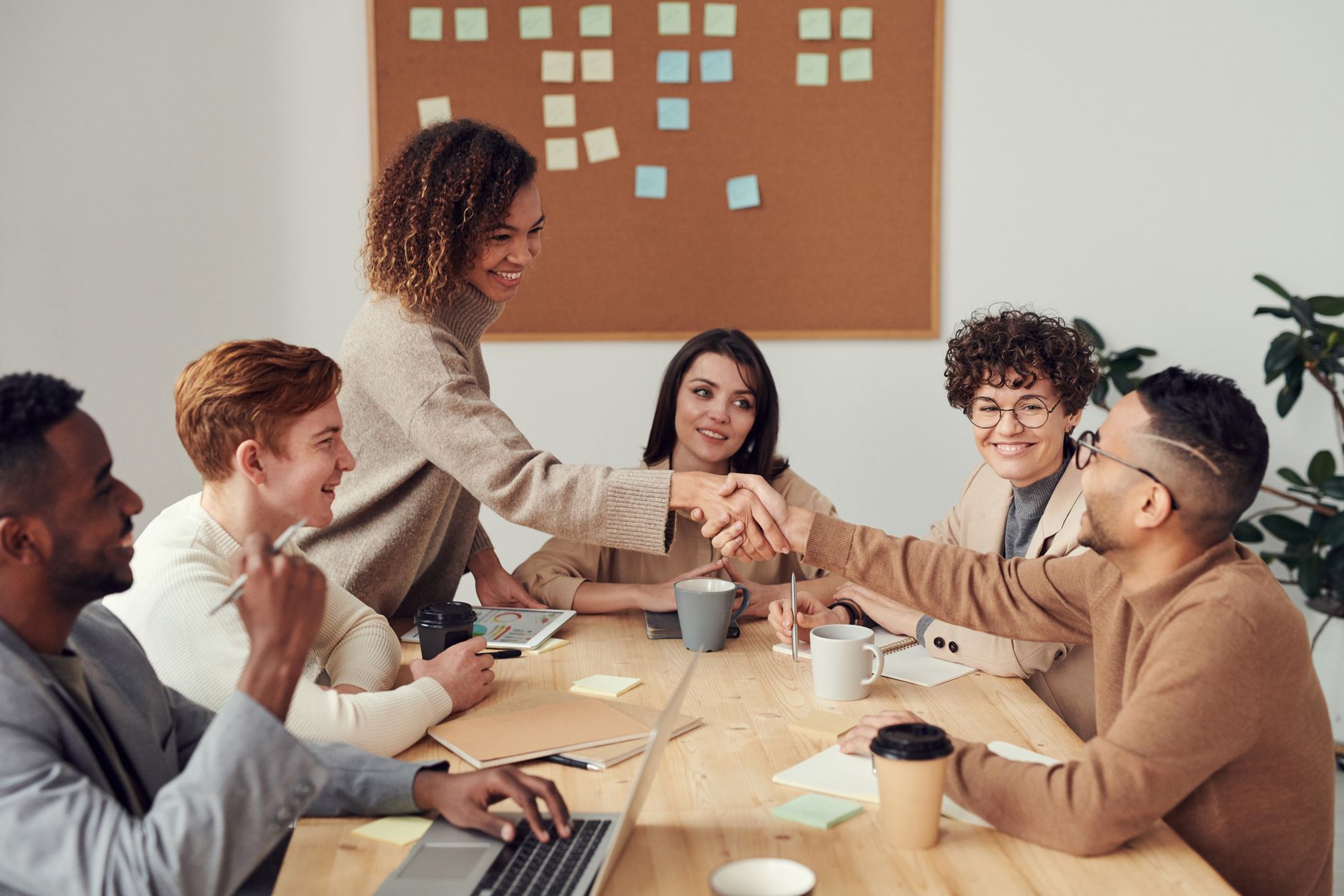 A diverse team around a table, one person standing and shaking hands with a colleague